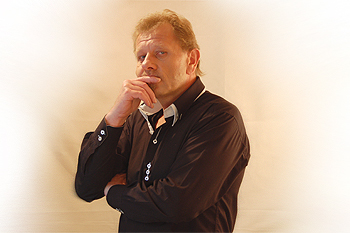 Der Mann auf diesem Foto fühlt eine Angriff seines Gesprächspartners. Die Schulter ist seitlich geneigt, um weniger Angriffsfläche zu bieten, der linke Arm schützt den Bauchbereich. Der Zeigefinger der rechten Hand liegt über den Mund, das zeigt das negative Gefühl und gleichzeitig eine Zurückhaltung, „ich sage nichts dazu“. Der Blick richtet sich zweifelnd nach links unten. Das Gehirn speichert in der linken Hemisphäre auch negative Erinnerungen,  Steffen H. Winterfeld, Mimik, Gestik,  Körpersprache, Kommunikation, Foto:  Erika Winterfeld 